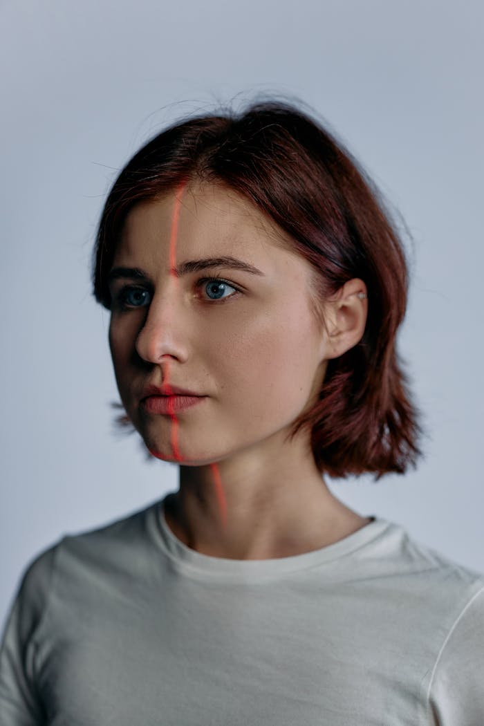 A futuristic portrait of a young adult woman with red laser lines on her face in a neutral studio setting.